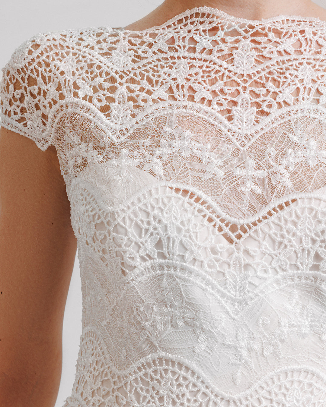 A close-up of a short-sleeves white evening dress in embroidered lace.