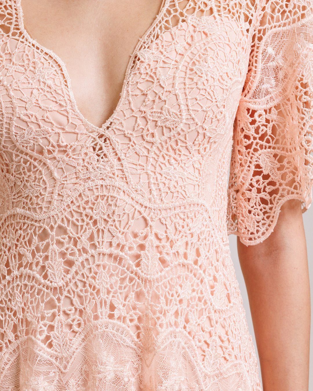 A close-up of a v-neckline lace evening dress in peach color with short bell sleeves.