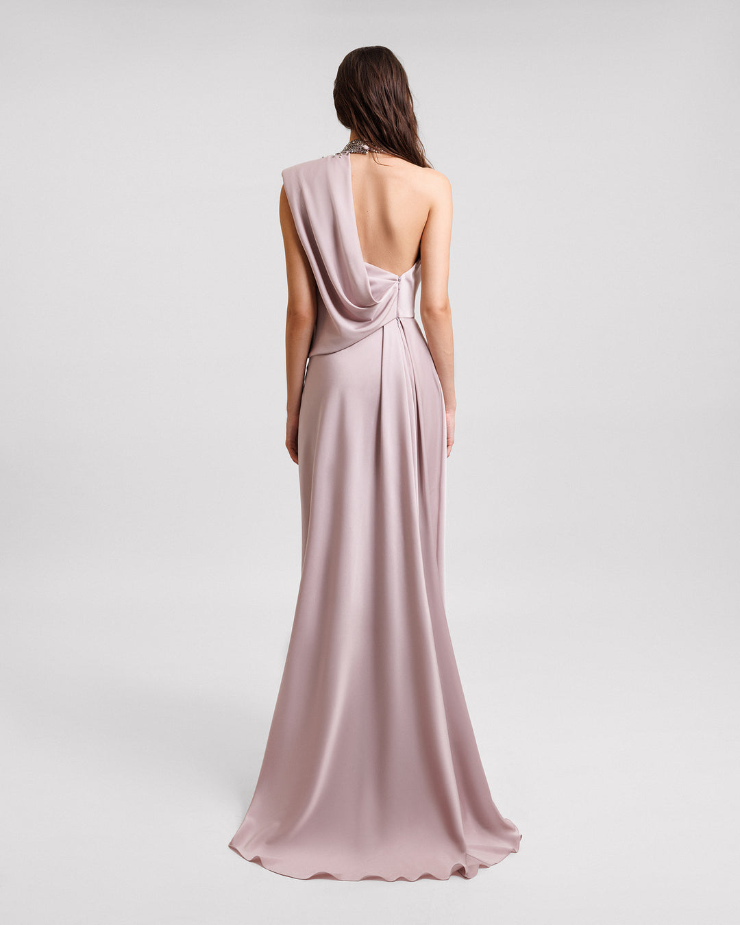 The back of a draped asymmetrical neckline evening dress in dusty pink satin with a stone embellished collar and an asymmetrical open back.