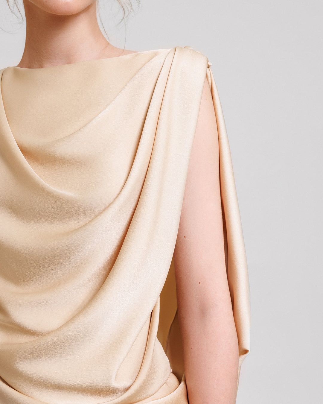 A close-up of an asymmetrical draped evening dress in champagne satin fabric.