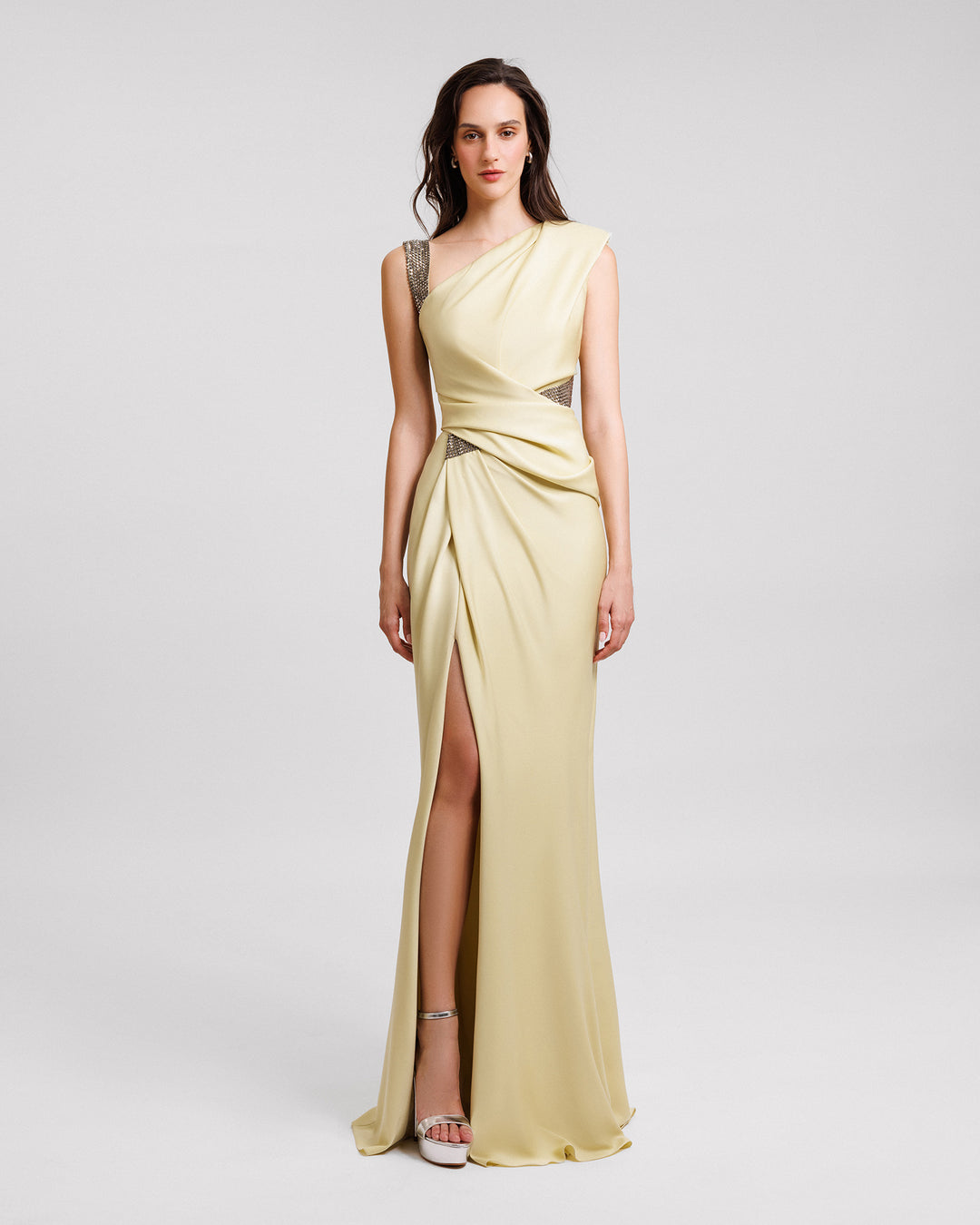 An asymmetrical neckline evening dress in pale lime color with stone embellished straps, draping, and an open slit.