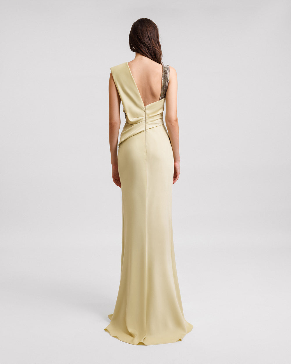 An asymmetrical open back evening dress in pale lime color with stone embellished straps and draping on the bodice.