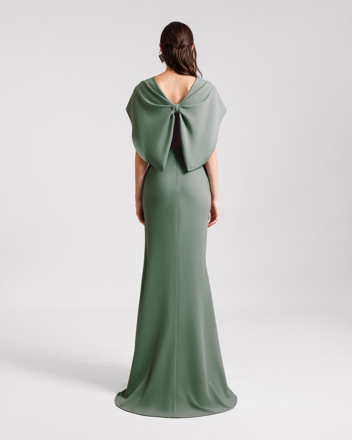 The back of a draped evening dress in sage color with cape-like sleeves and a bow design at the back.