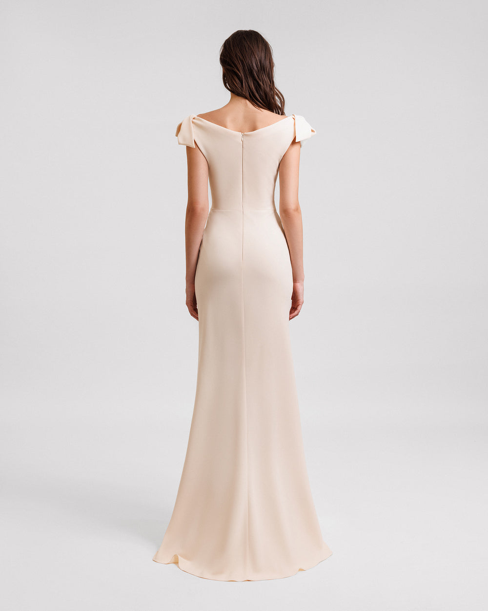 The back of a long evening dress in cream color crepe with bows on the shoulders.