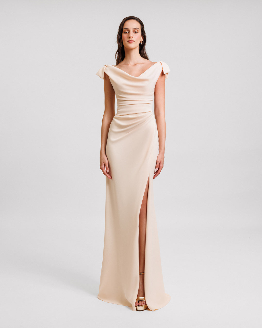 A long evening dress in cream color crepe with a draped corset, cowl neckline, bows on the shoulders and an open slit on the side.