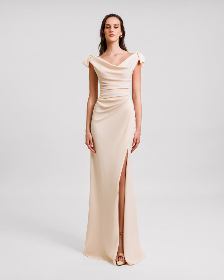 A long evening dress in cream color crepe with a draped corset, cowl neckline, bows on the shoulders and an open slit on the side.