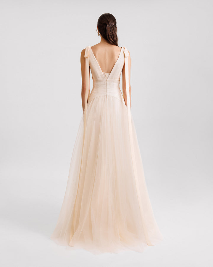 The back of a V-cut open back evening dress in cream tulle with bows on the shoulders and a draped waistline.