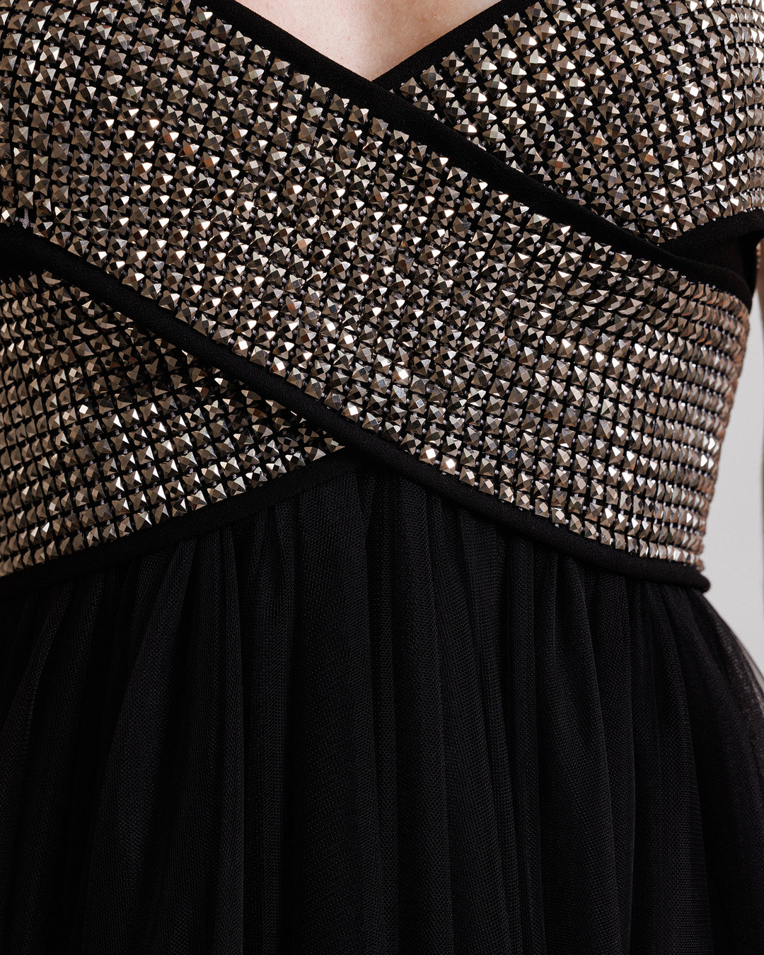 A close-up of a black evening dress in tulle with a bow-like stone embellished top.