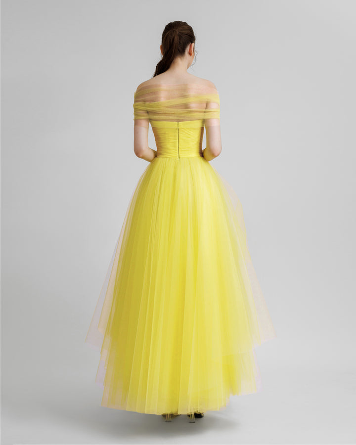 The back of an off-shoulder yellow tulle dress with an asymmetrical lower part.