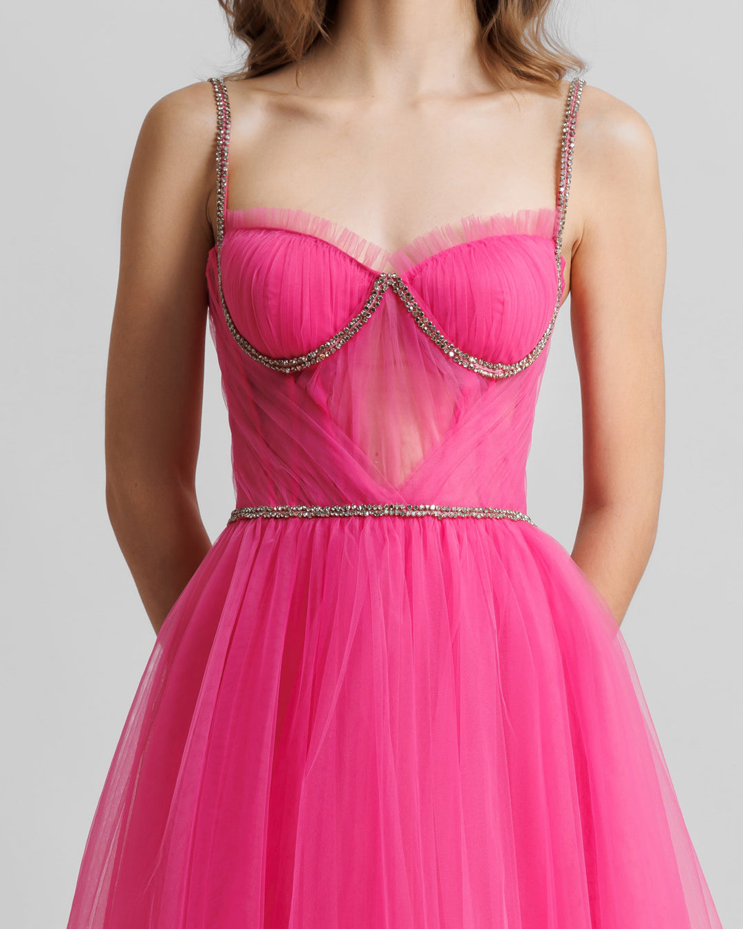 A close-up of a fuchsia tulle dress featuring beaded straps and a draped corset.