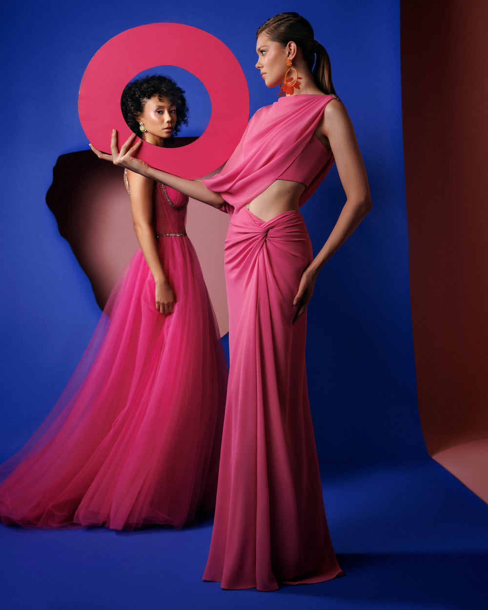 An asymmetrical pink evening dress with a draped sleeve, cut out on the waist, draped skirt, and a slit on the side.