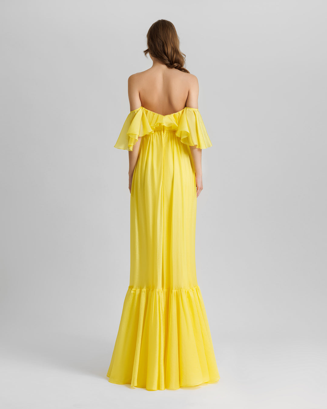 The back of a ruffled off-the-shoulders flowy yellow evening dress with a draped hemline.