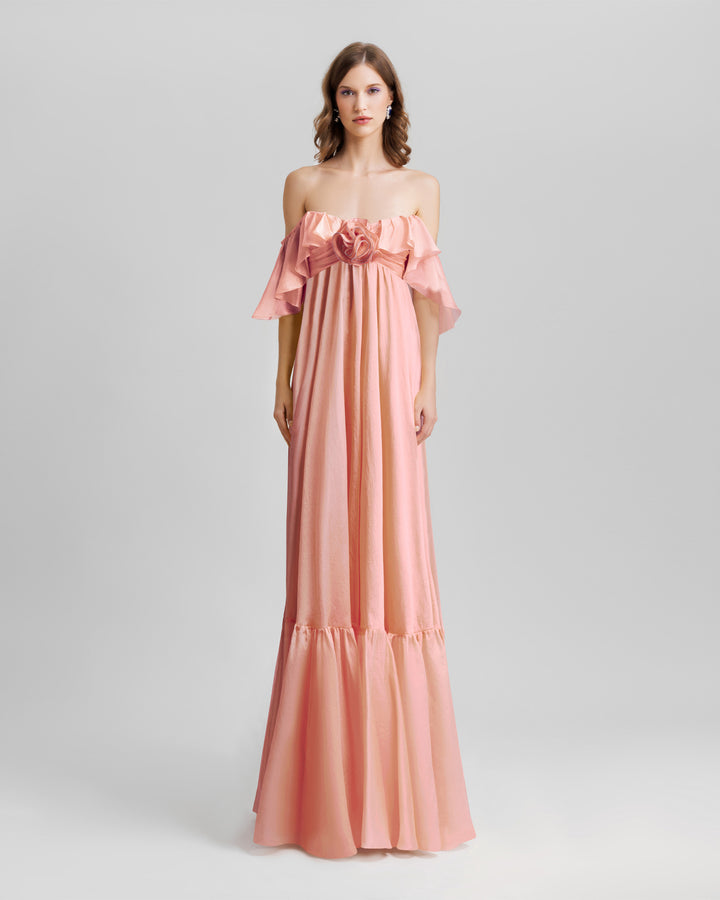 A ruffled off-the-shoulders flowy dress in salmon color with a draped flower at the front.