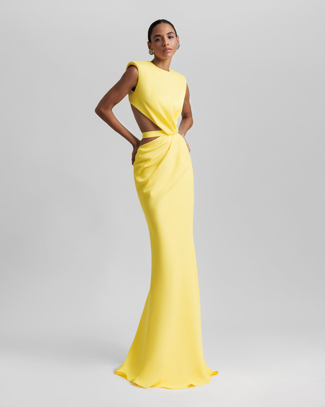 A slim-cut yellow dress featuring padded shoulders, draping and cut-outs on the waist, and an open back.