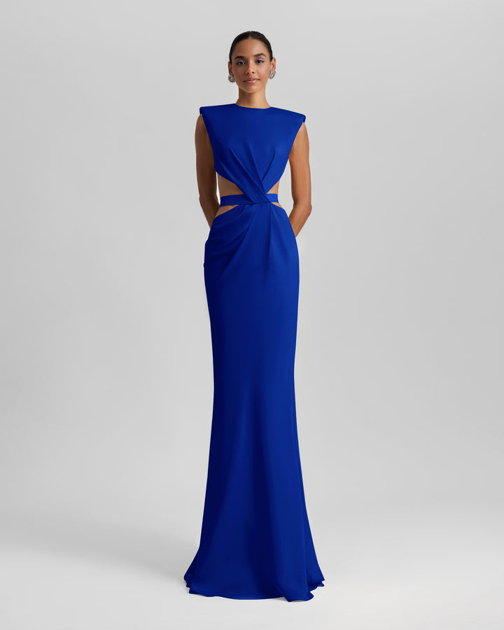 A slim-cut royal blue evening dress featuring padded shoulders, draping and cut-outs on the waist, and an open back.