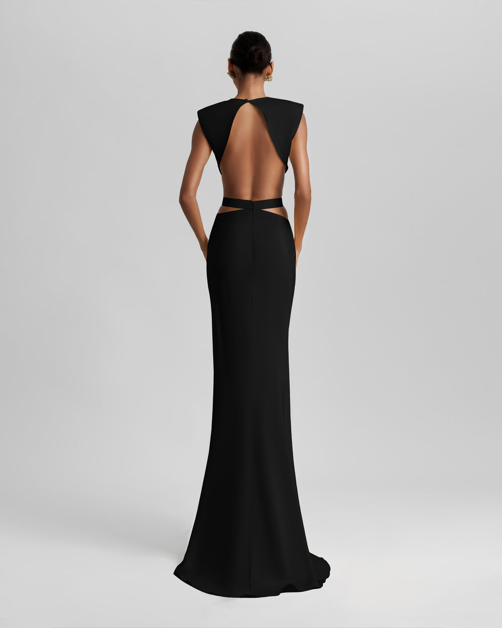 The back of a slim-cut black dress featuring padded shoulders, cut-outs on the waist, and an open back.