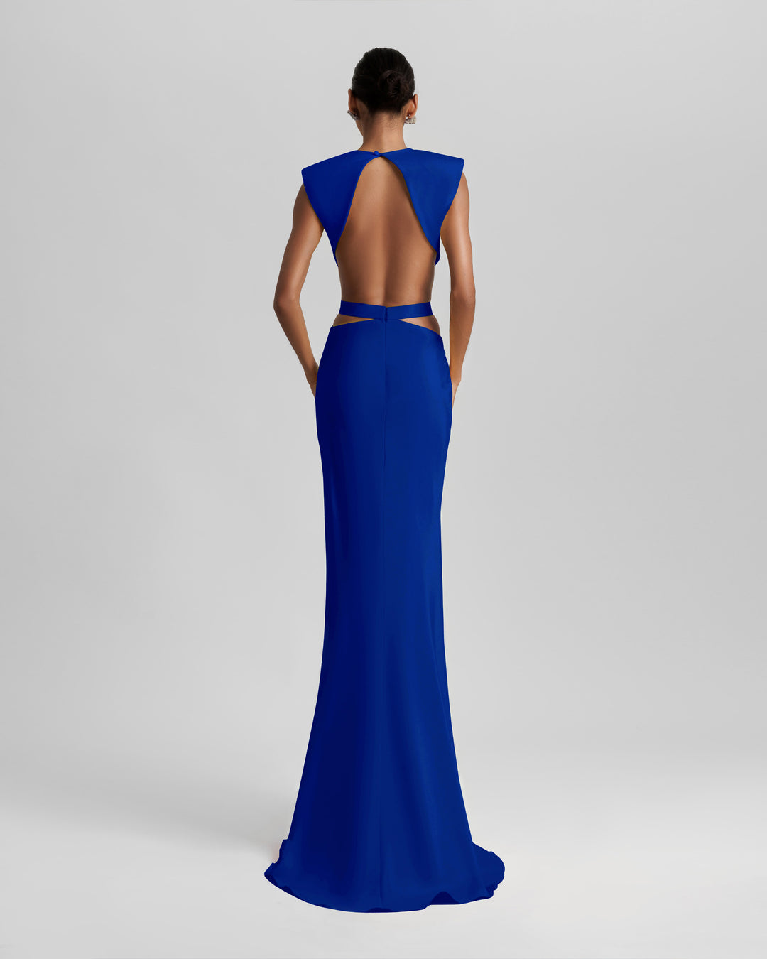 The back of a slim-cut royal blue evening dress featuring padded shoulders, draping and cut-outs on the waist, and an open back.