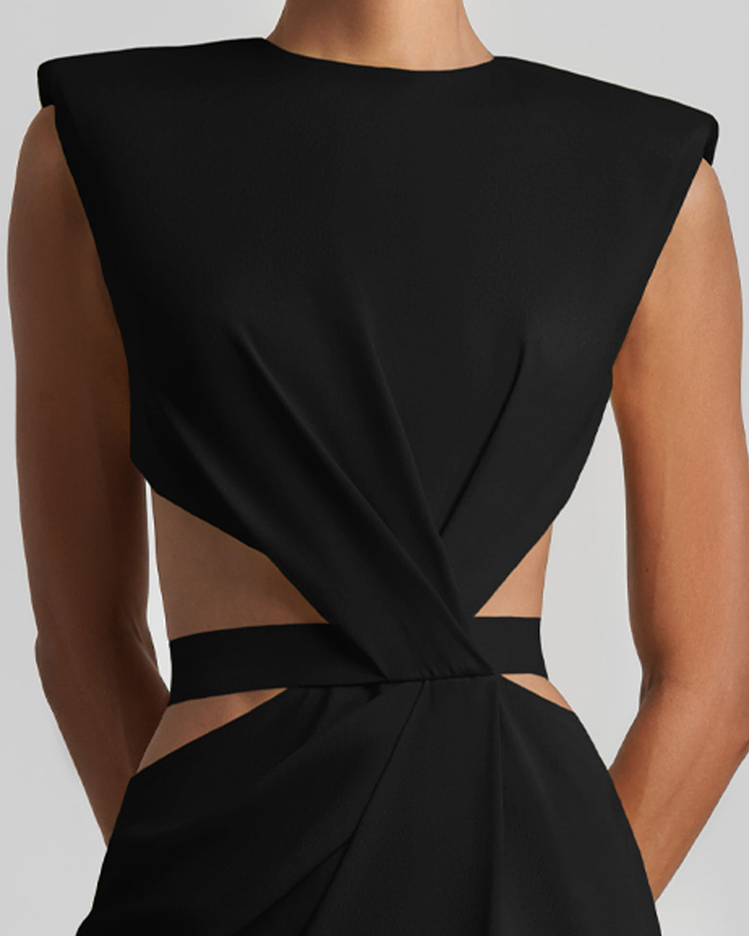 A close-up of a slim-cut black dress featuring padded shoulders, draping, and cut-outs on the waist.