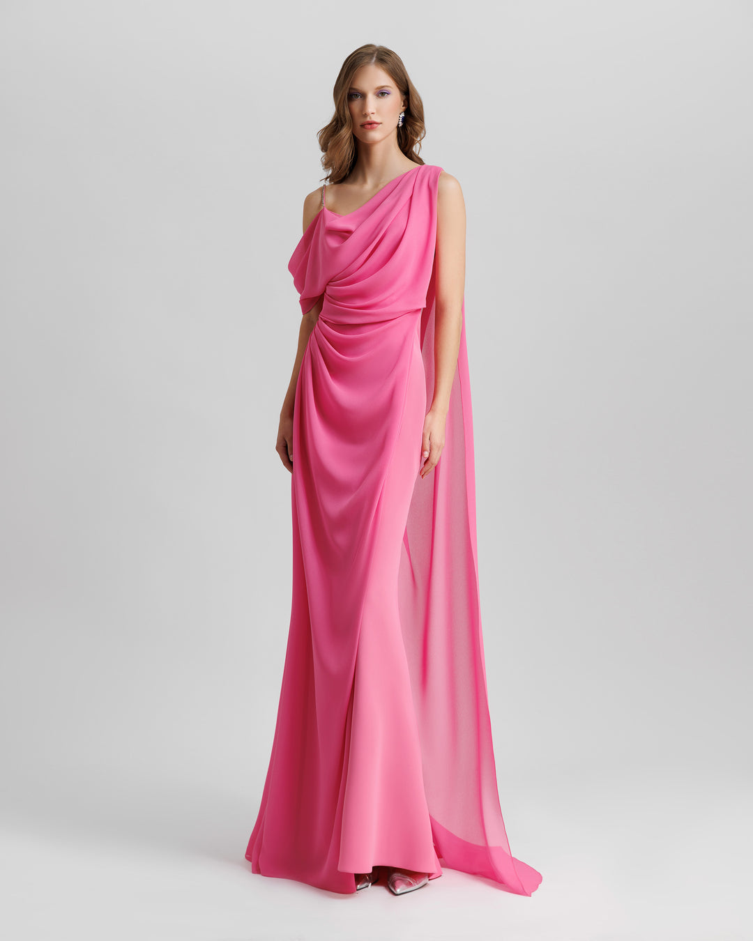 An asymmetrical neckline, one-shoulder draped pink evening dress with a dropped cape at the back.