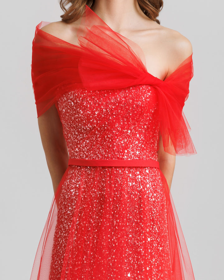 A close-up of an off-the-shoulders red tulle dress with a beaded underlayer and a bow design.