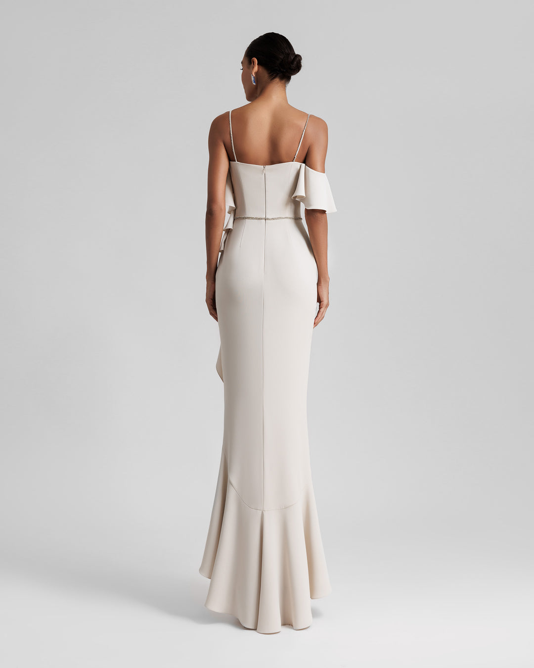 The back of a long off-shoulders champagne evening dress, featuring thin bedazzled straps, built in belt and ruffle details from the bust going all the way down to the hemline.