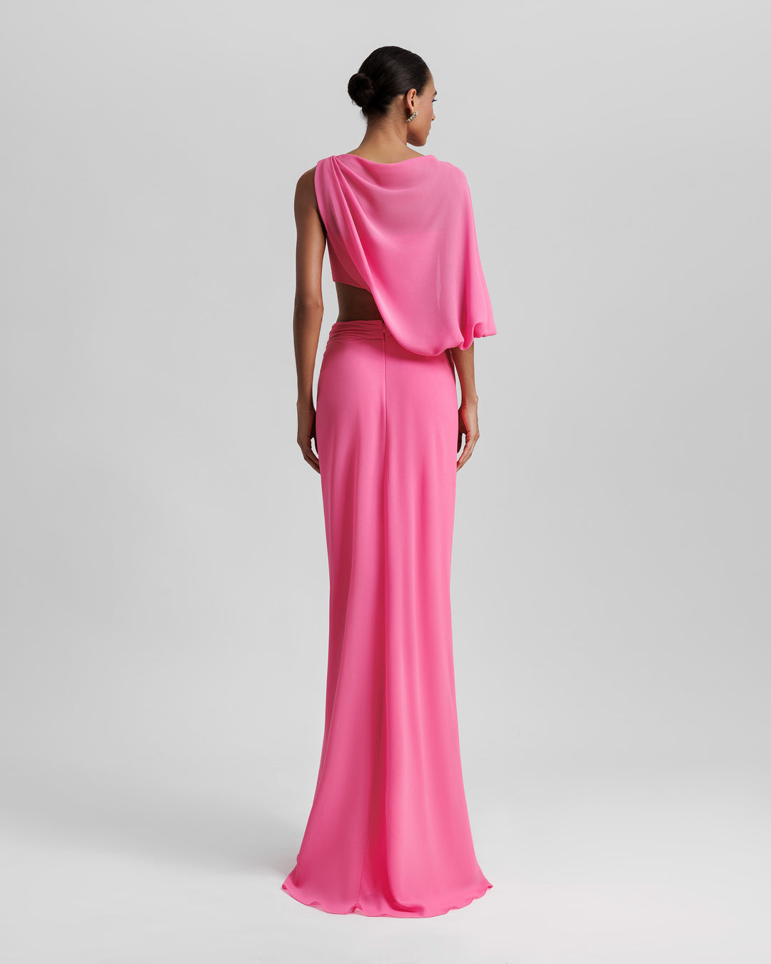 The back of an asymmetrical pink evening dress with a draped sleeve and a cut out on the waist.