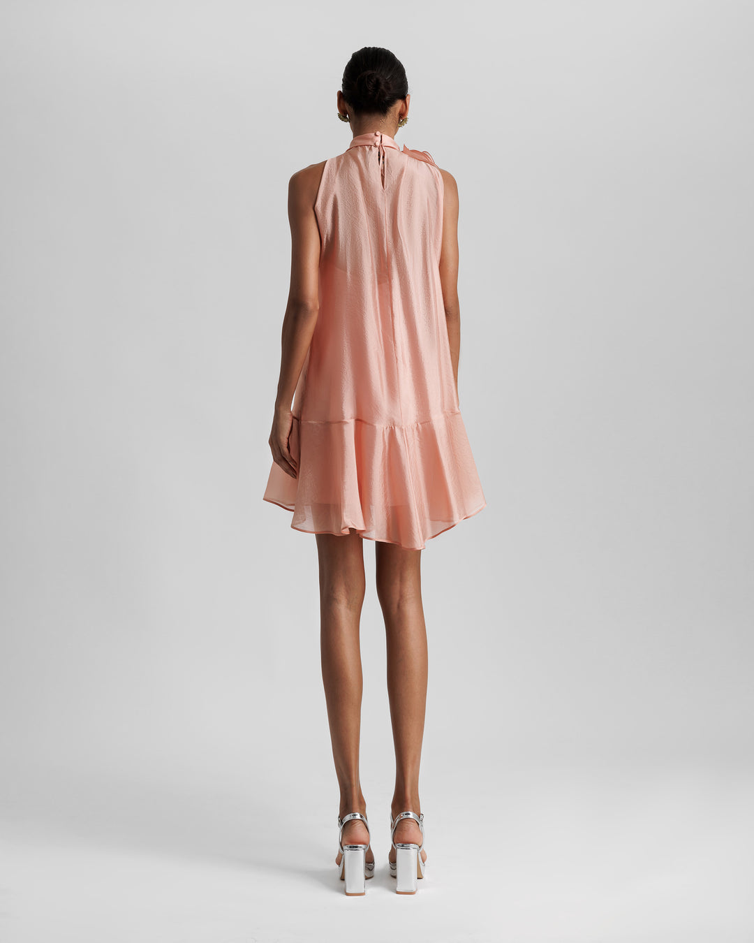 The back of a high-collar short dress in salmon color with ruffled hemline.