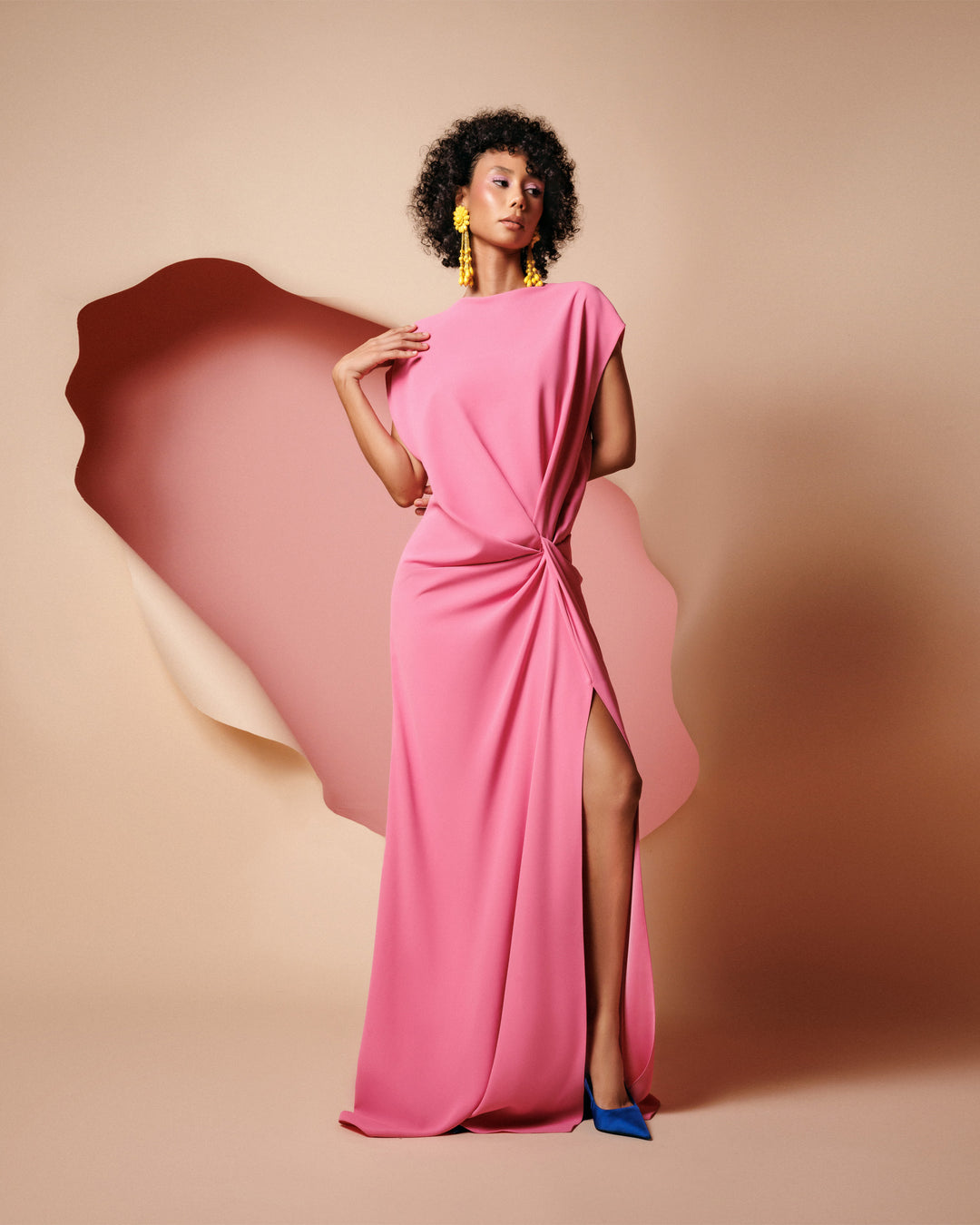 A loose-cut pink evening dress with draping at the waist and a slit on the side.