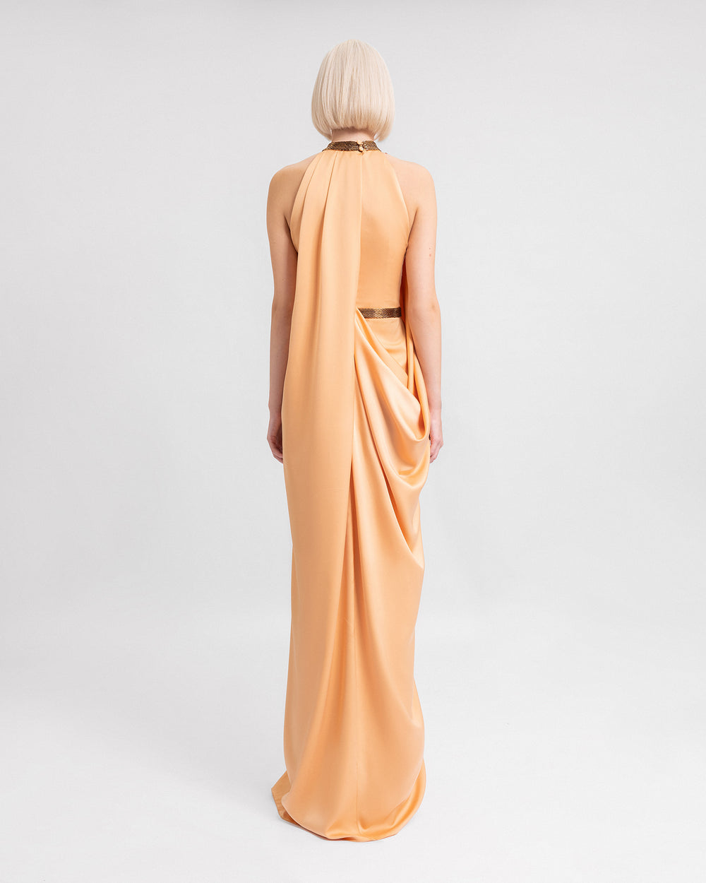 The baCK OF a loose-cut evening dress in peach satin featuring a beaded collar and belt, and draping on the back.