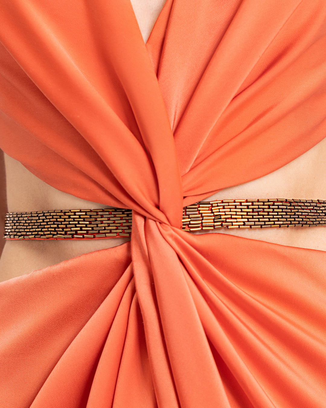 A close-up of a draped coral satin evening dress with a beaded belt.