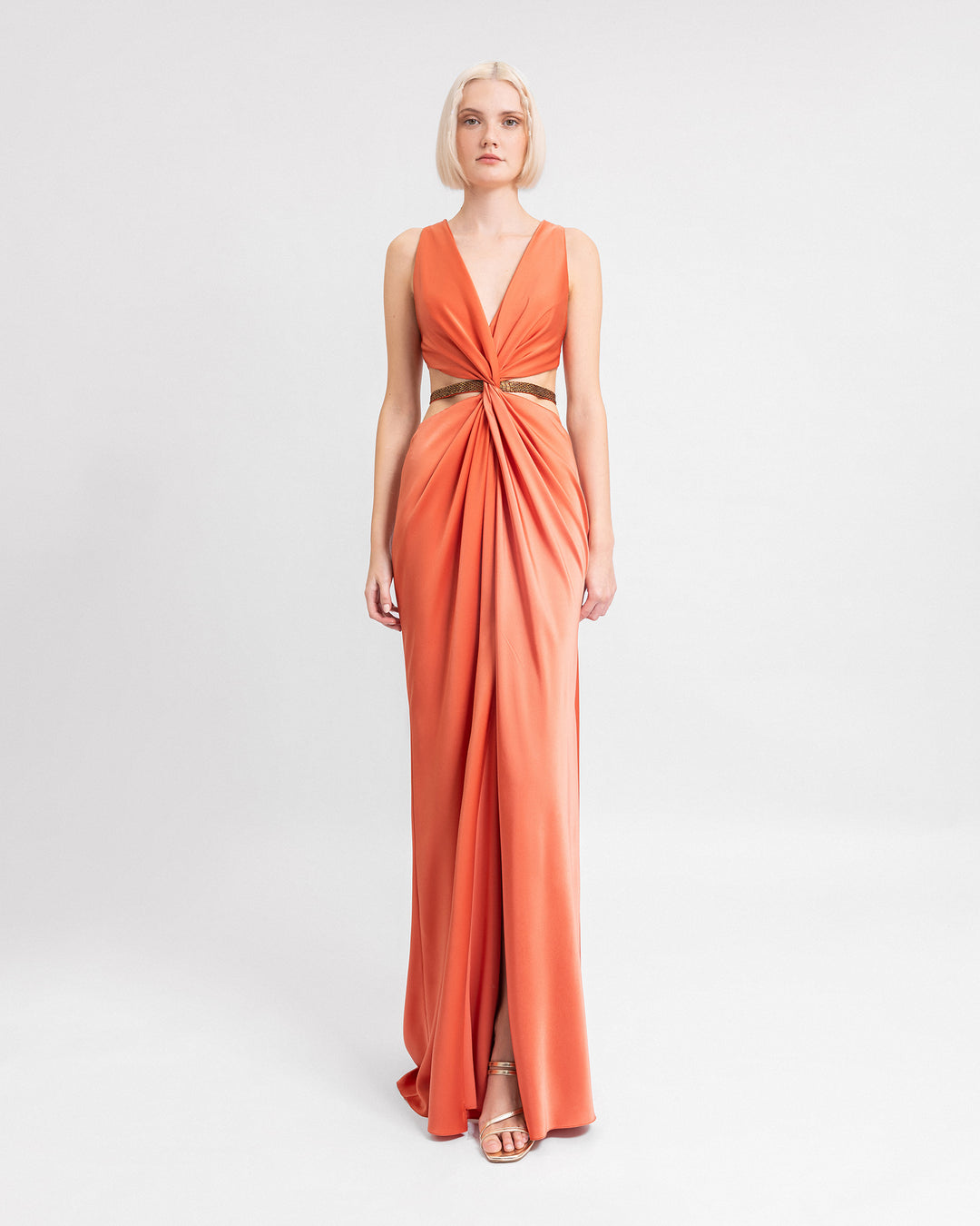 A v-neckline draped evening dress in coral satin with a beaded belt.