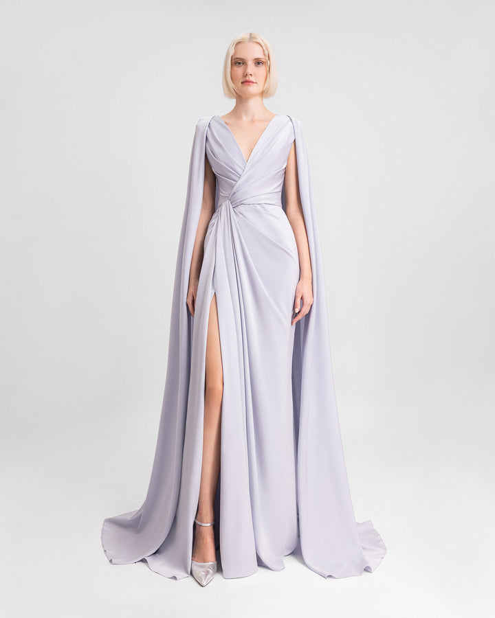 A V-neckline draped evening dress in ice blue satin fabric with cape-like sleeves and a slit on the side.