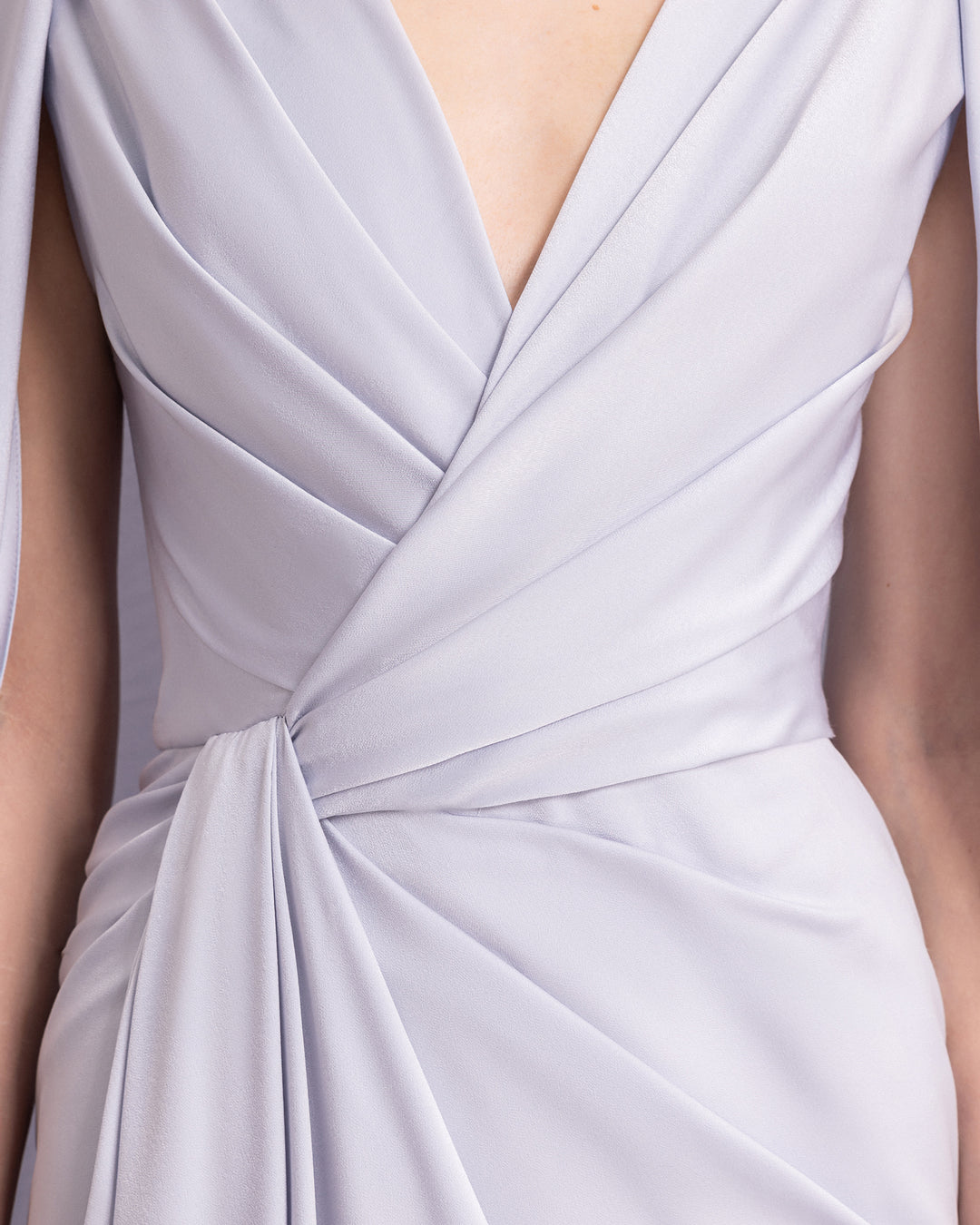 A close-up of a V-neckline draped evening dress in ice blue satin fabric with cape-like sleeves.