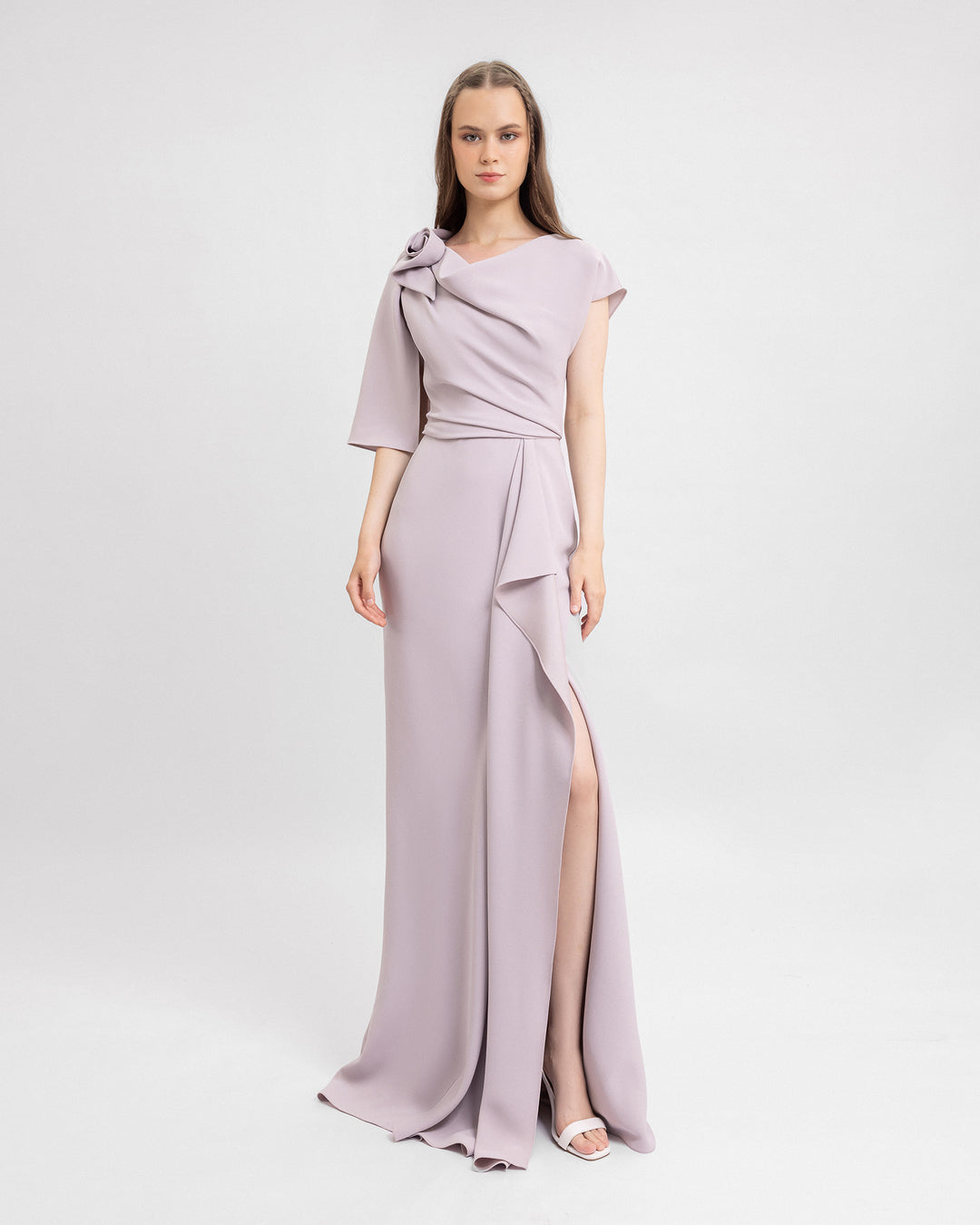 A draped evening dress in dusty pink featuring asymmetrical sleeves and a ruffled slit on the side.