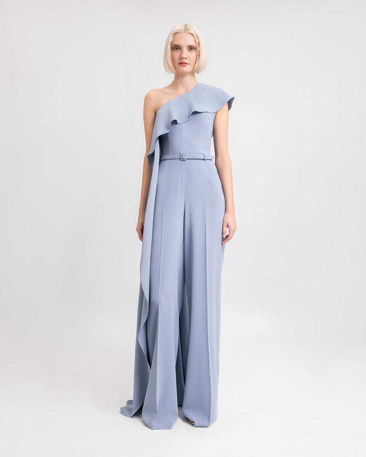 A one-shoulder straight-cut jumpsuit in dusty blue with a long ruffled neckline and a detachable belt.