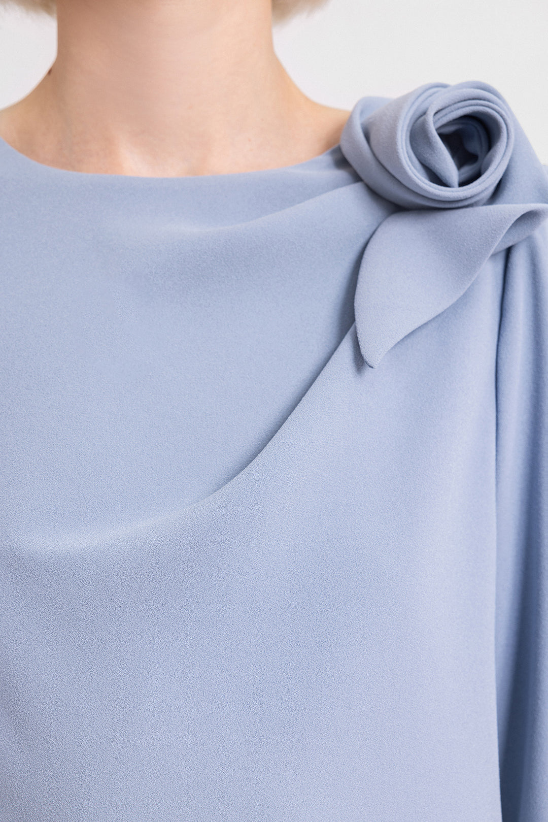 A close-up of a loose-cut evening dress in dusty blue with a draped flower on the shoulder.