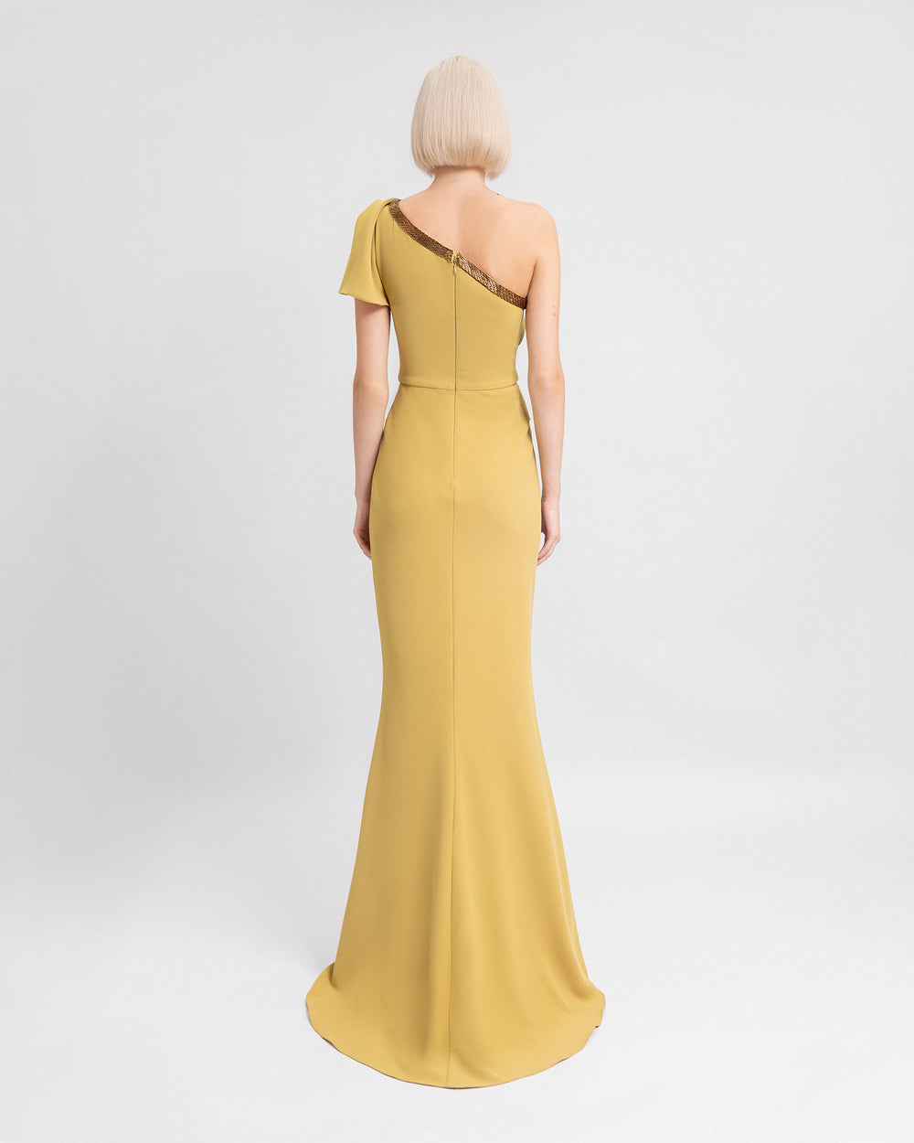 The back of a one-shoulder draped evening dress in mustard with beadings on the neckline.