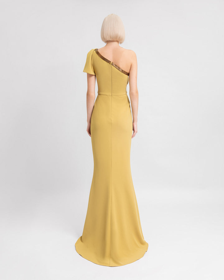 The back of a one-shoulder draped evening dress in mustard with beadings on the neckline.