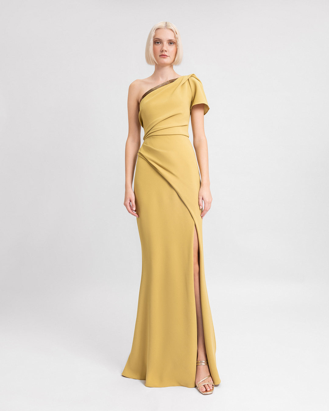 A one-shoulder draped evening dress in mustard with beadings on the neckline and an open slit on the side.