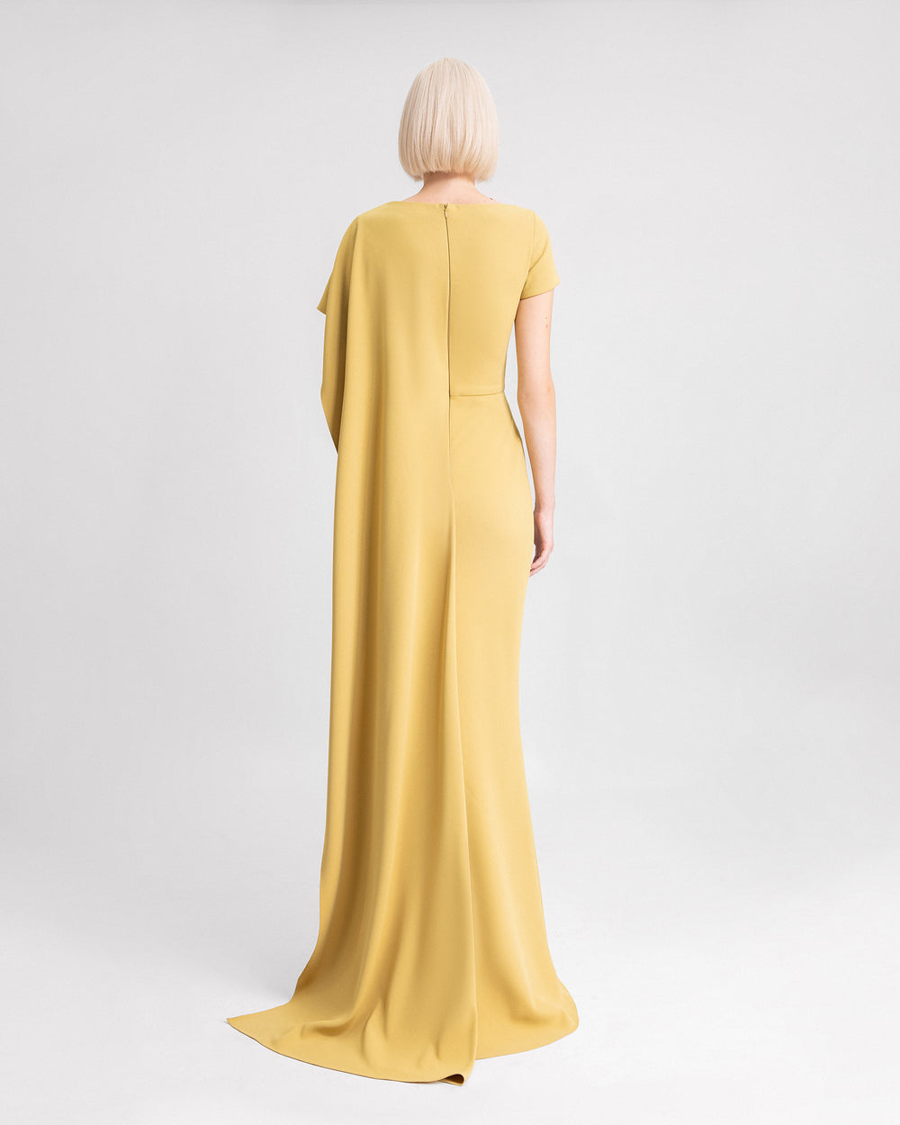 The back of a mustard evening dress featuring draping on the waistline and a long ruffled cape-like sleeve.