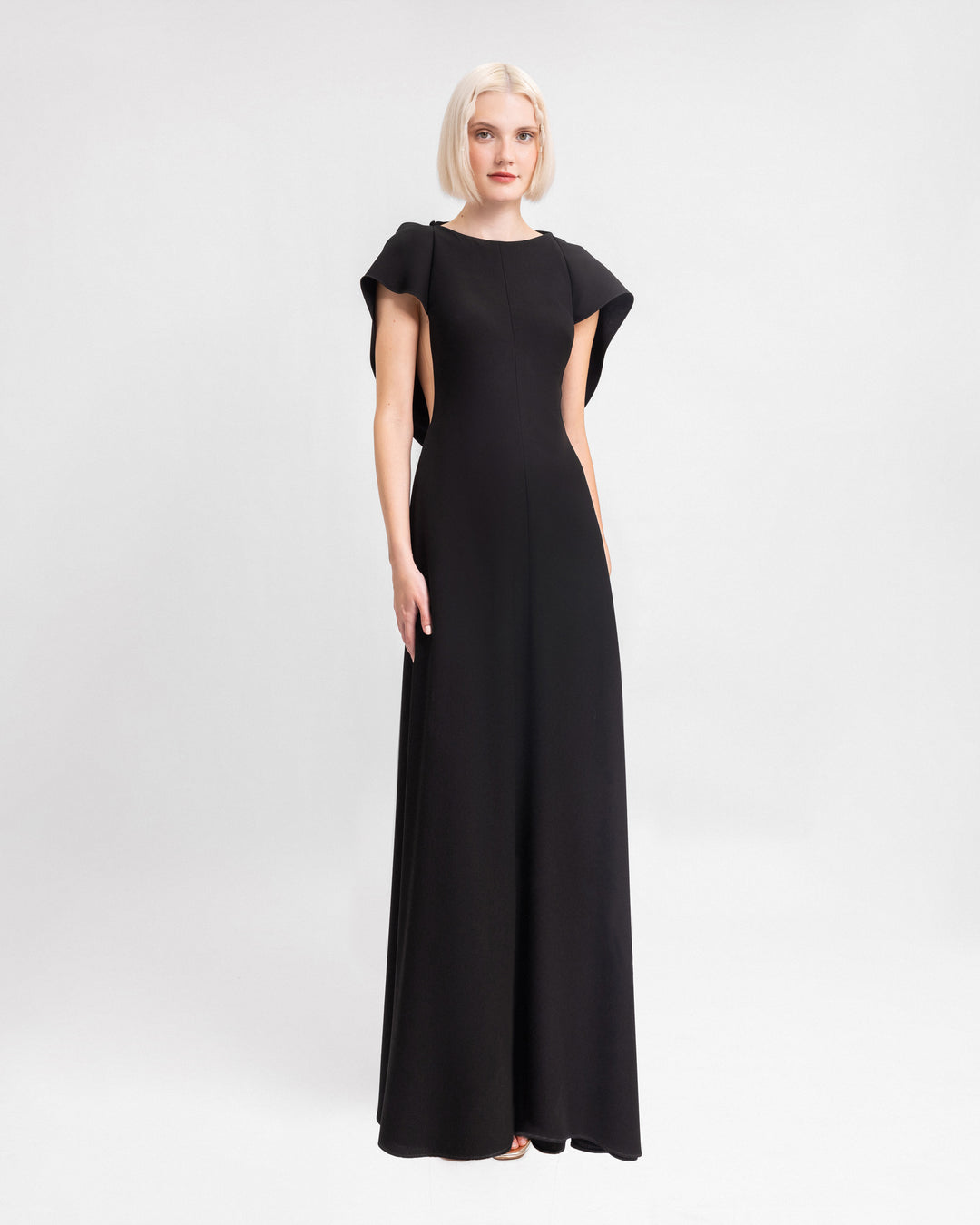 A long black evening dress with draped sleeves and a cut-out at the back.