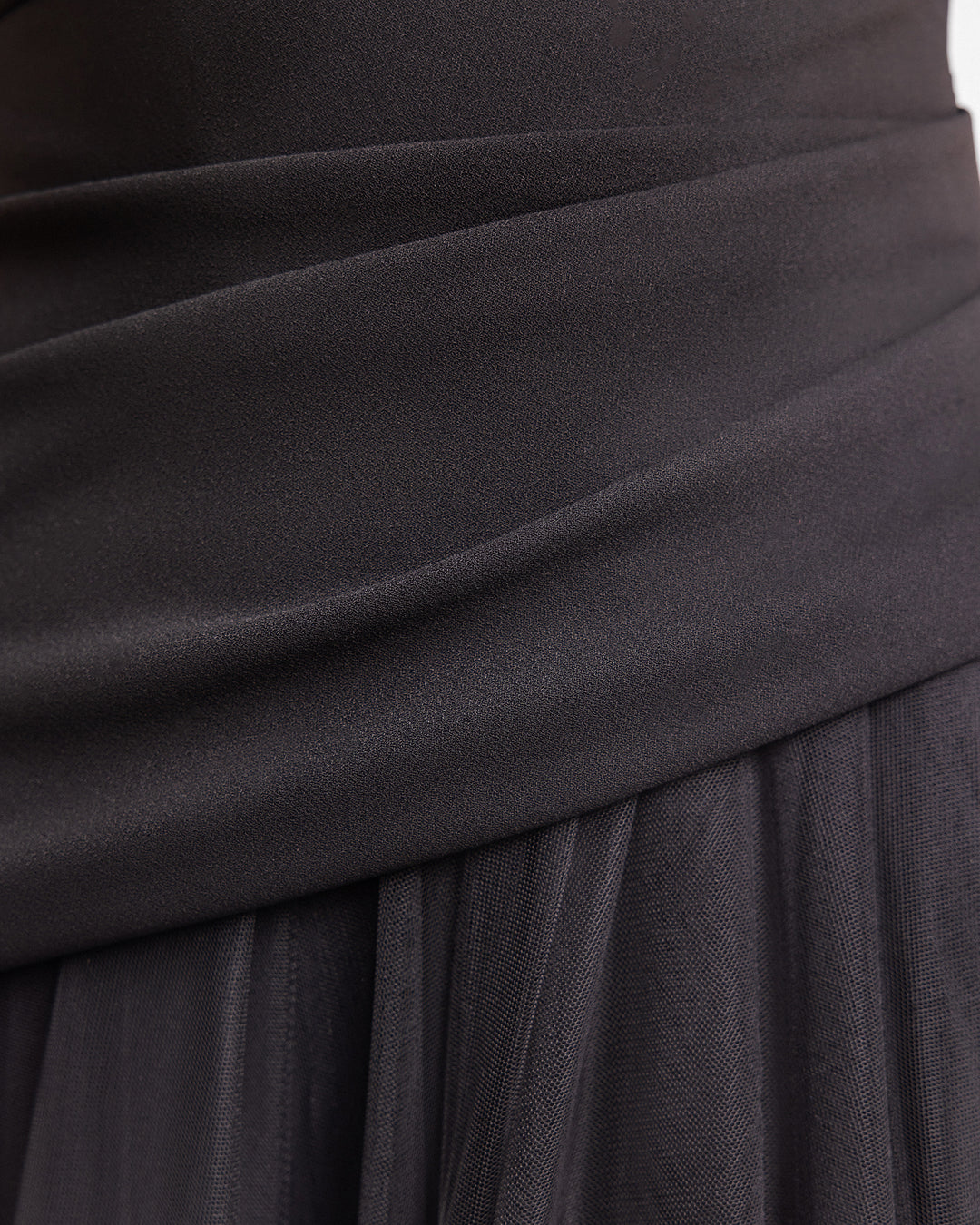 A close-up of black crepe evening dress with an asymmetrically draped corset and a tulle skirt.