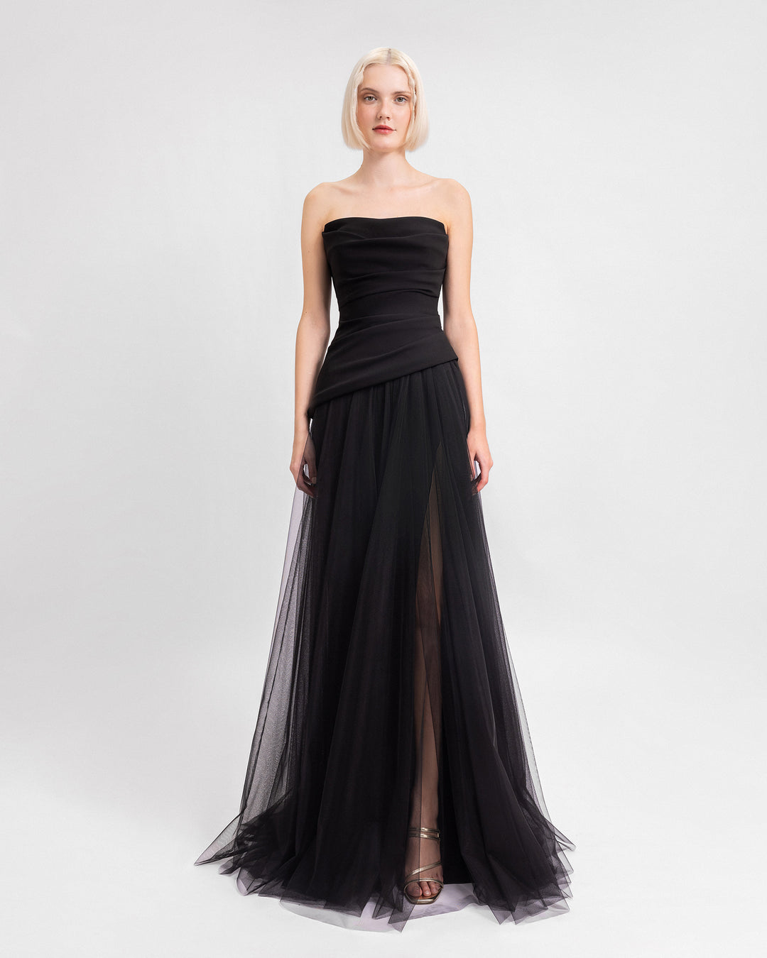 A strapless black evening dress with an asymmetrically draped corset and a tulle skirt with a slit on the side.