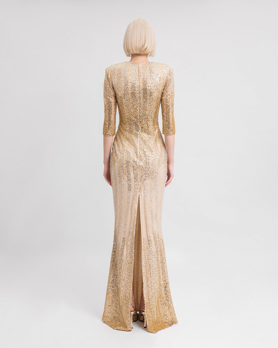 The back of a fully beaded long golden evening dress with three-quarter sleeves and a slit at the back.