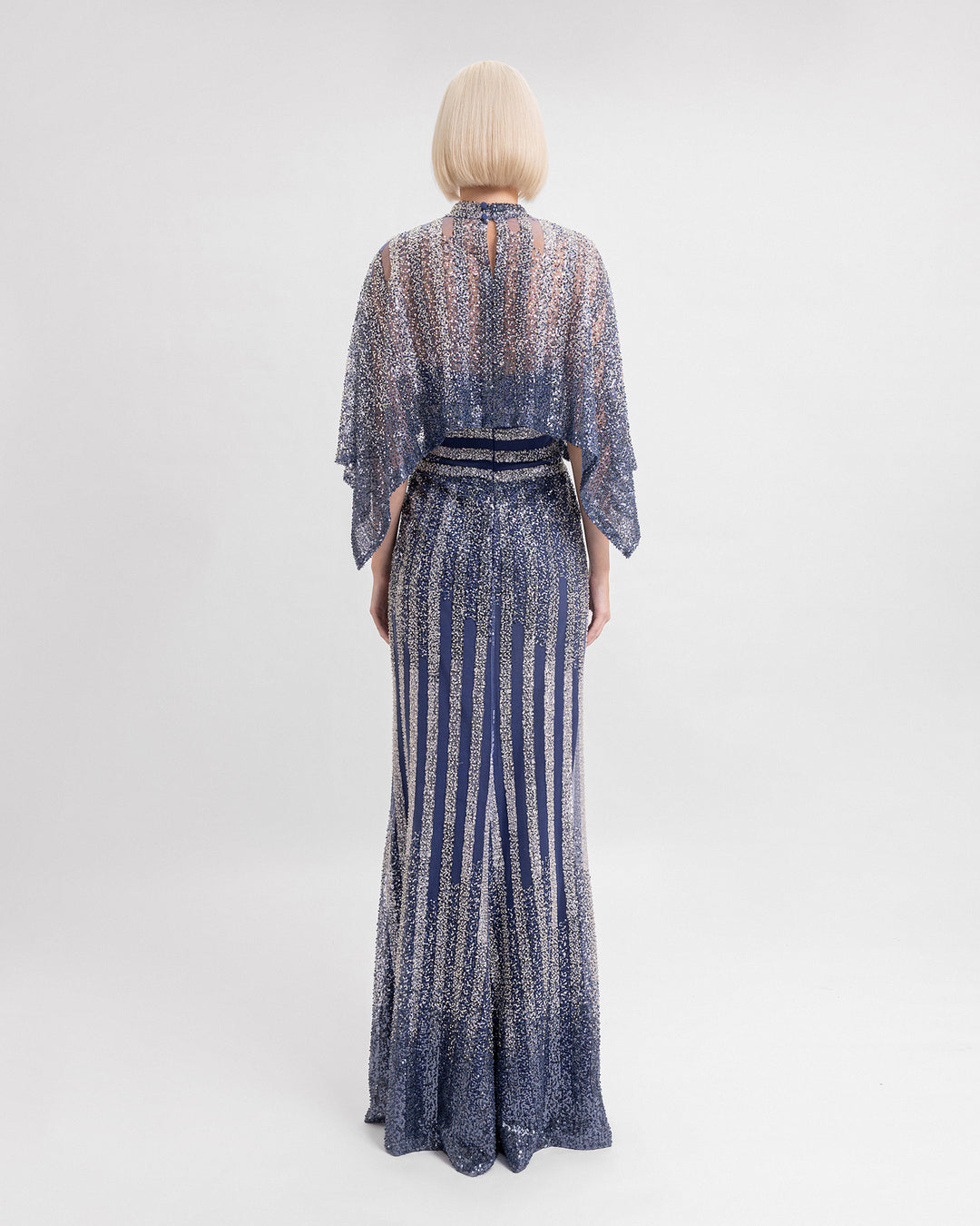 The back of a long beaded sequins dress in navy hues with cape-like sleeves.