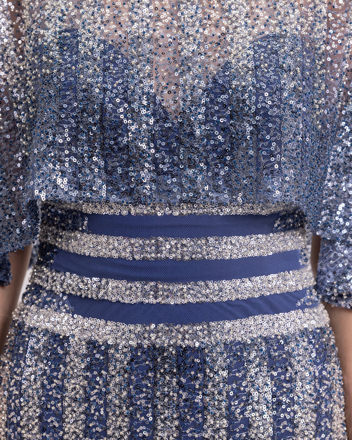 A close-up of a long beaded sequins dress with cape-like sleeves.