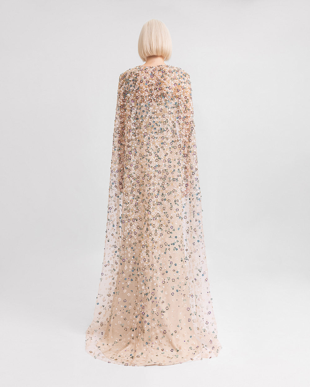 The back of a strapless draped evening dress in beige crepe paired with a fully beaded long cape.