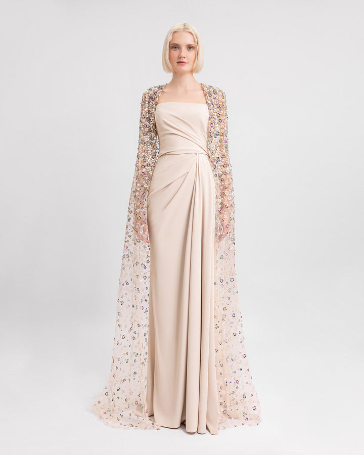 A strapless draped evening dress in beige crepe paired with a fully beaded long cape.