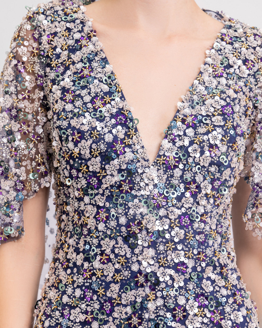  close-up of a V-neckline fully beaded evening dress with cape-like sleeves and a slit at the front.