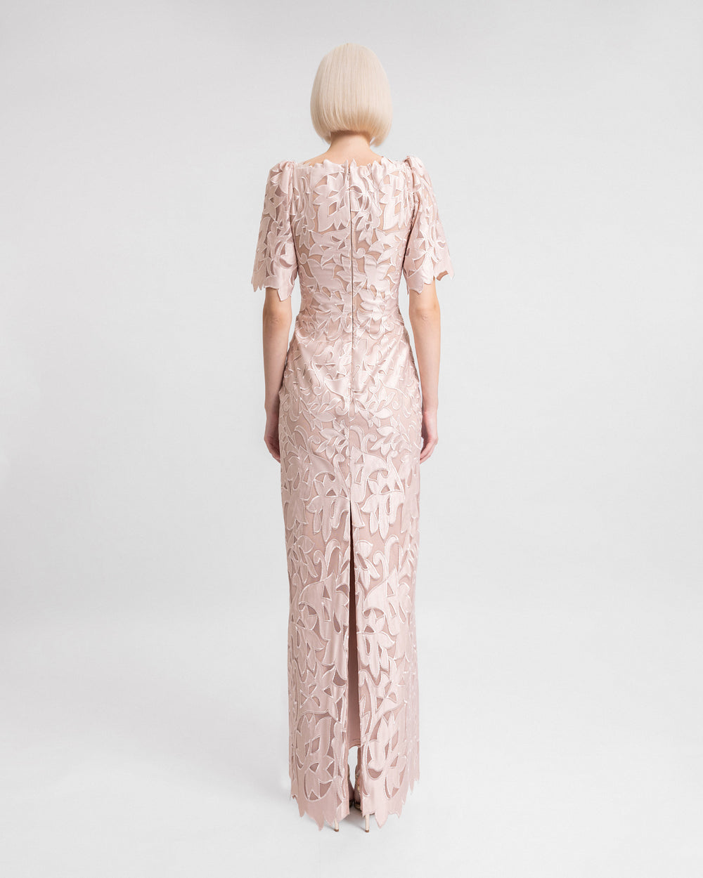 The back of an embroidered satin long evening dress in blush color with puffed sleeves and a slit at the back.